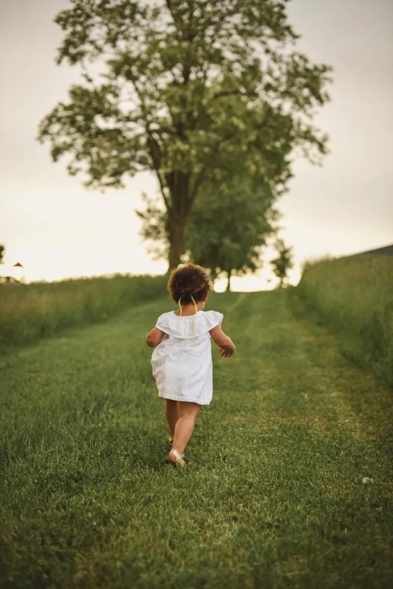 A young child running along a grassy path towards a tree